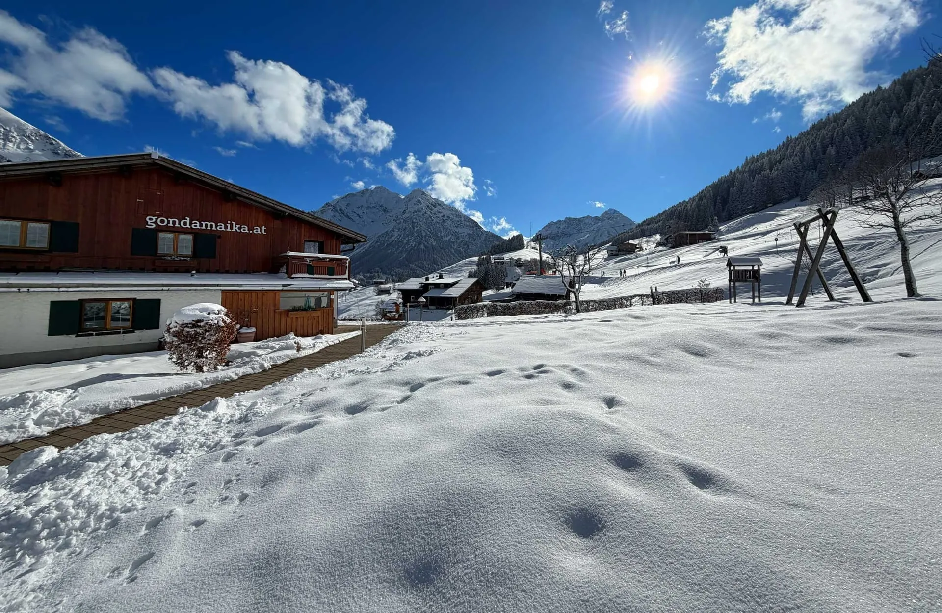Verschneiter Garten und Bergpanorama mit blauem Himmel rund um das Walserhaus Gondamaika in Hirschegg, Kleinwalsertal