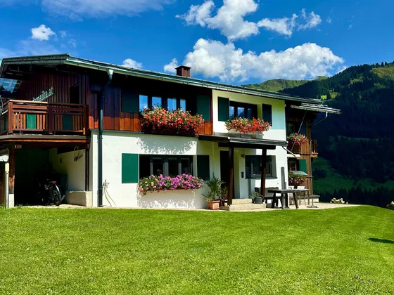 The Gondamaika house in summer with flowering balcony boxes and a mountain backdrop