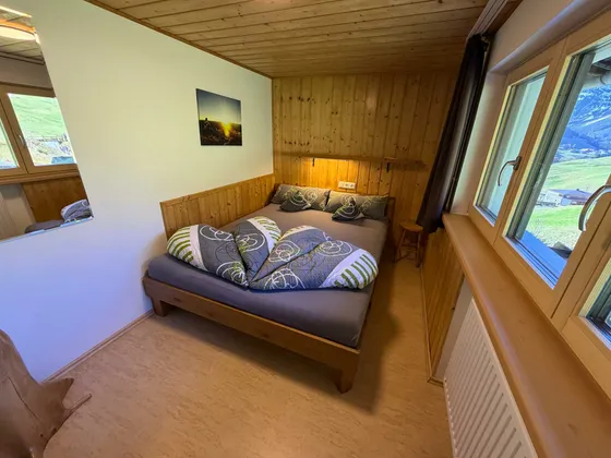 Slaapkamer 2 met bed van 160 cm onder een houten cassetteplafond en groene gordijnen