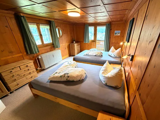 Slaapkamer 2 met twee grote bedden onder een houten cassetteplafond en groene gordijnen