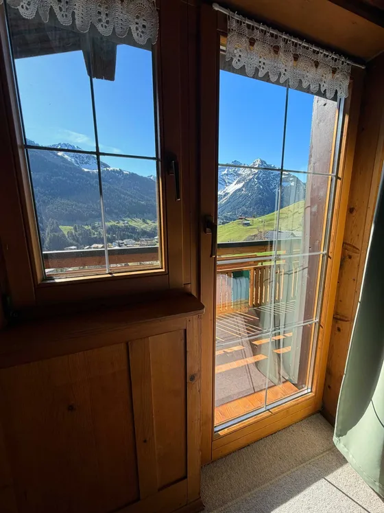 Ochtendzon in slaapkamer 2 van Appartement 22 — zicht door de balkondeur op de besneeuwde toppen van Kleinwalsertal