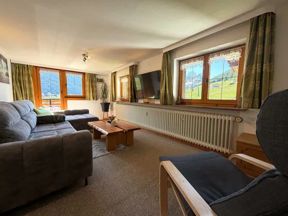 Woonkamer van Appartement 22 met tv en raampartij naar het bergpanorama